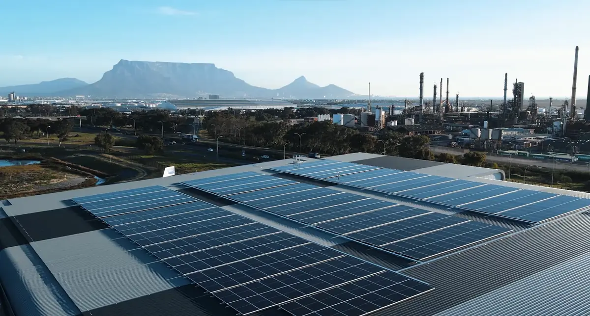 Rooftop solar array on an industrial roof, with mountains and a plant in the background